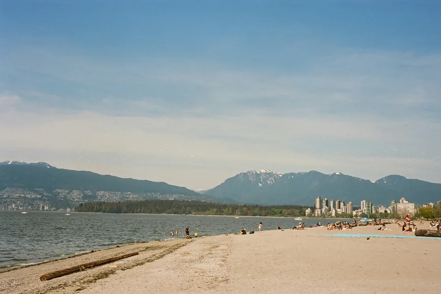 People sitting on a beach beside the water with Vancouver in the background