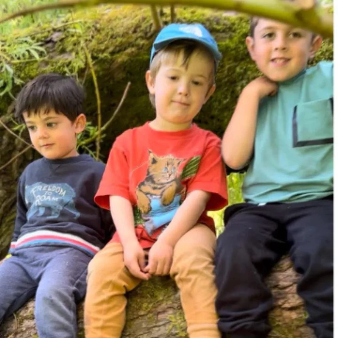 Children sitting on a mossy log during outdoor summer camp.