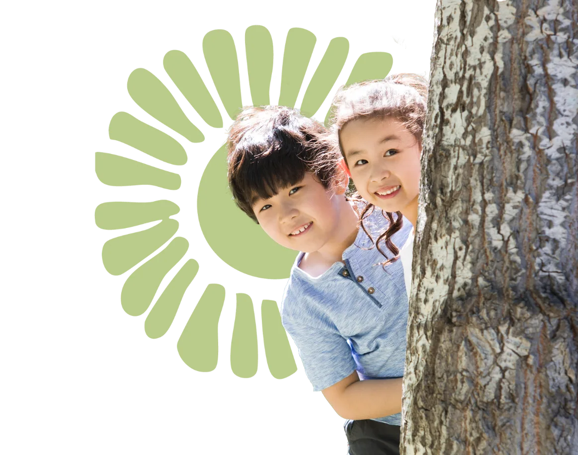 Children smiling from behind a tree.
